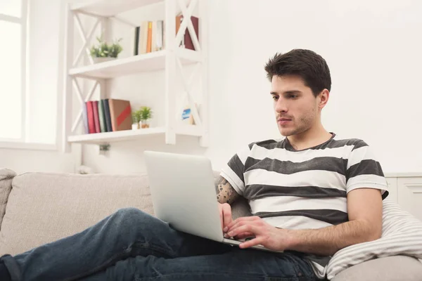 Hombre joven en casa de mensajería en línea en el ordenador portátil — Foto de Stock