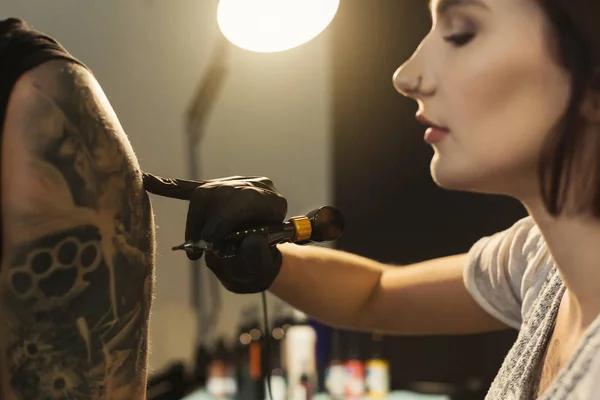 Young woman tattooist doing tattoo on shoulder