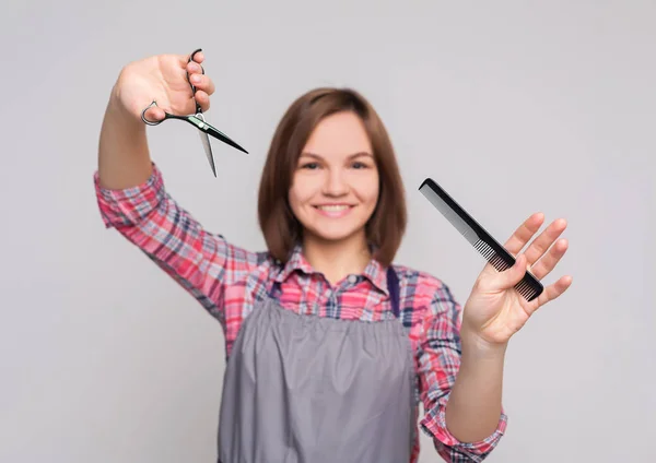 Жіночий перукар тримає ножиці і гребінець на сірому фоні — стокове фото