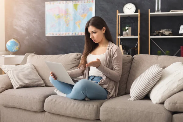 Mujer conmocionada usando el ordenador portátil mientras está sentado en el sofá — Foto de Stock