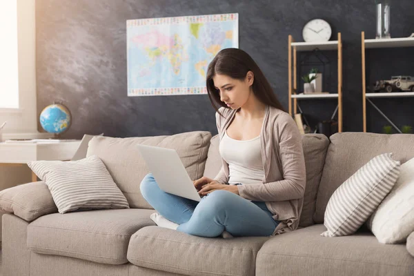 Mujer seria usando el ordenador portátil mientras está sentado en el sofá — Foto de Stock
