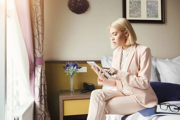 Businesswoman sitting on bed and using tablet