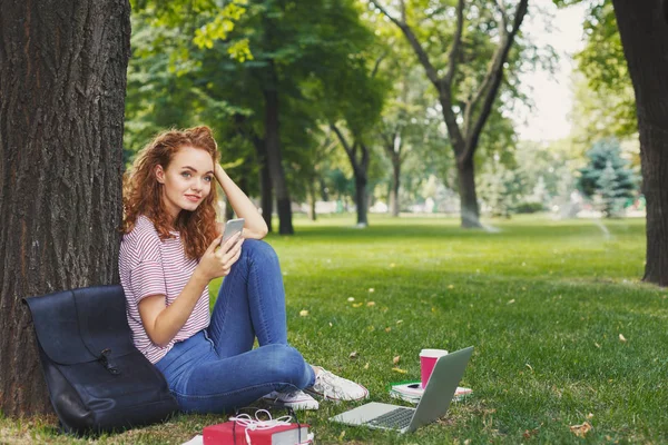 Feliz joven mujer mensajes de texto en el teléfono inteligente en el parque —  Fotos de Stock