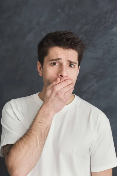 Uomo spaventato che copre la bocca con mano su sfondo grigio — Foto Stock