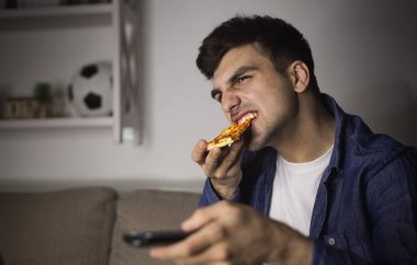 Pizza yemek ve uzaktan kumanda tutan adam