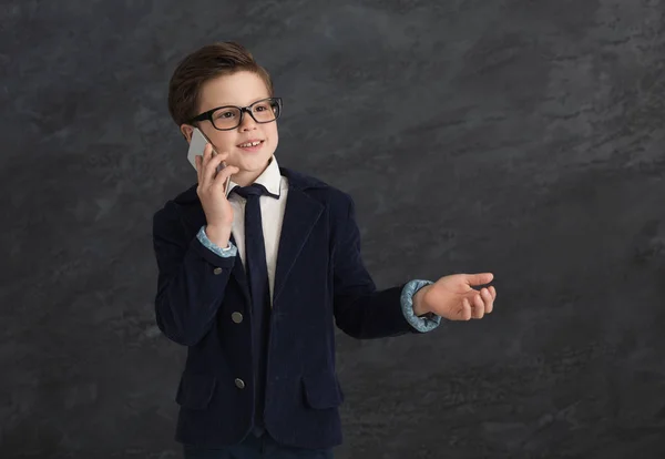 Kleiner Junge im Anzug spricht auf Handy vor grauem Hintergrund — Stockfoto