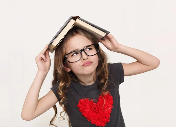 Menina pensativa com livro sobre a cabeça no fundo branco — Fotografia de Stock