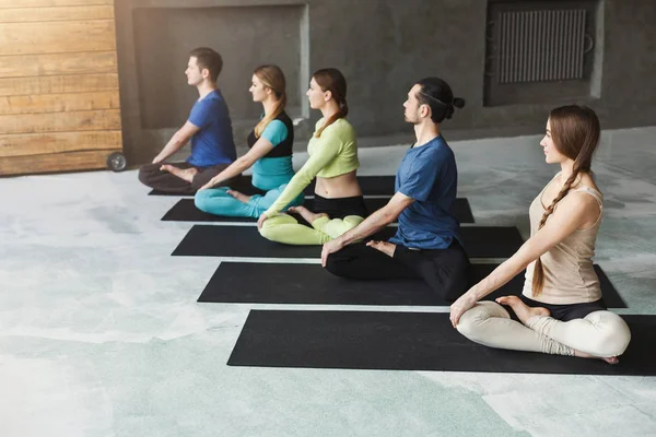 Unga kvinnor och män i yogaklass, koppla av meditation pose — Stockfoto
