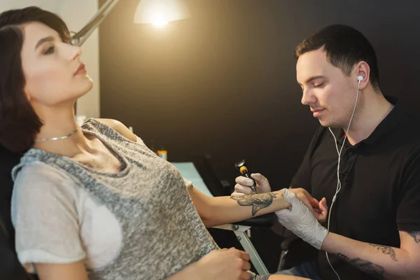 Tattoo artist working with needle on clients arm