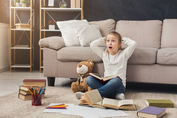 Pequeña niña leyendo libro mientras está sentada en la alfombra —  Fotos de Stock