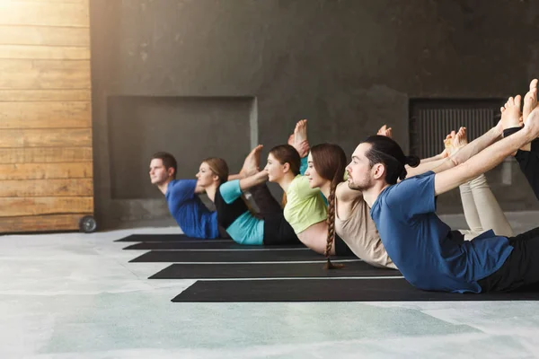 Mujeres y hombres jóvenes en clase de yoga, haciendo ejercicios de estiramiento — Foto de Stock
