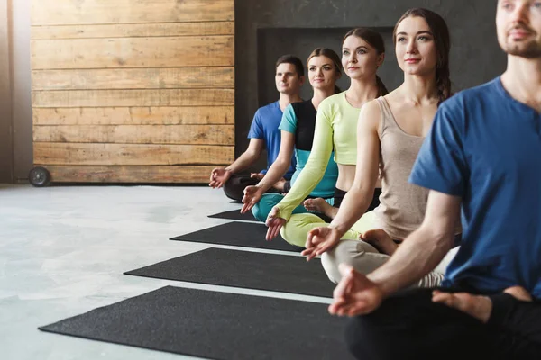 Giovani donne e uomini in classe di yoga, rilassarsi posa meditazione — Foto Stock