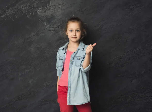 Kleines Mädchen zeigt Daumen nach oben vor grauem Hintergrund — Stockfoto