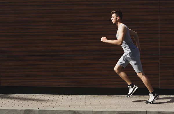 Young muscular man running in city, dark wooden wall background, copy space, side view