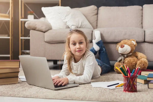 Aranyos kis lány csinál házi feladatot, laptop, feküdt a padlón — Stock Fotó