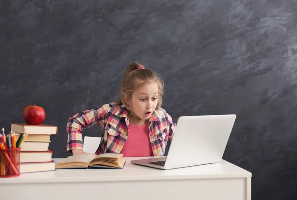 Mengejutkan gadis kecil melakukan pekerjaan rumah pada laptop — Stok Foto