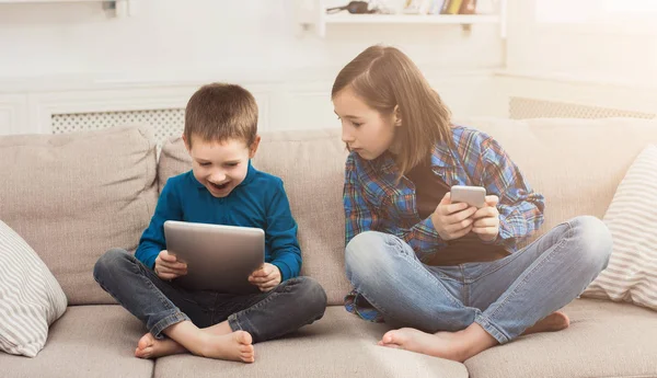 Twee kinderen met gadgets op de Bank thuis — Stockfoto