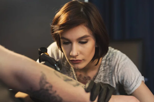 Young woman tattooist doing tattoo on male arm