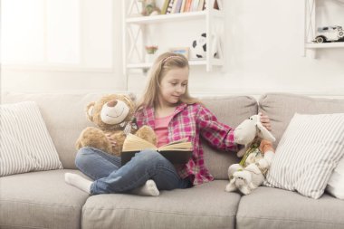 Mutlu küçük çocuk onun oyuncak ayı için kitap okuma