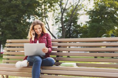 Mutlu genç kadın cep, laptop, hoş bir atmosfer açık havada parkta oturan çalışma freelancer söz. Teknoloji, iletişim, eğitim ve uzak çalışma kavramı, kopya alanı