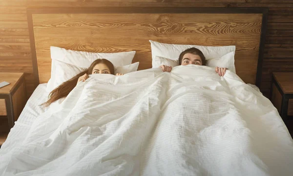Sorprendidos hombre y mujer escondidos bajo una manta en su cama en casa —  Fotos de Stock