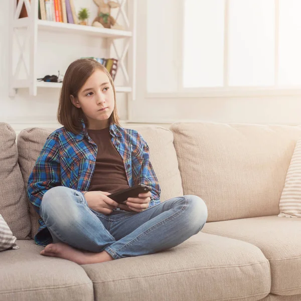 Young serious girl watching TV with remote control