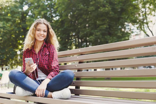 Hermosa mujer sentada y escuchando música en el teléfono inteligente ou — Foto de Stock