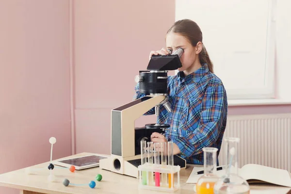 Colegiala mirando en el microscopio en la lección —  Fotos de Stock