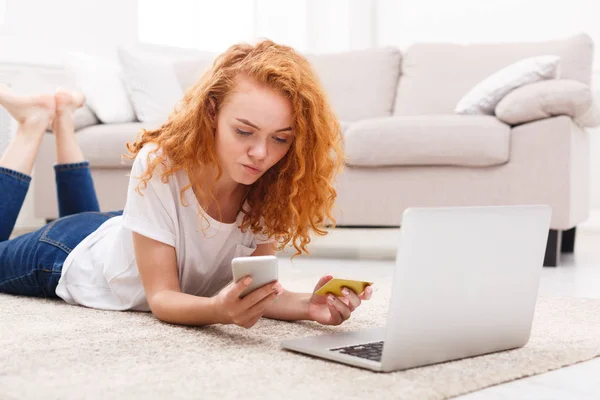 Pensive girl shopping online with laptop and phone — Stock Photo, Image