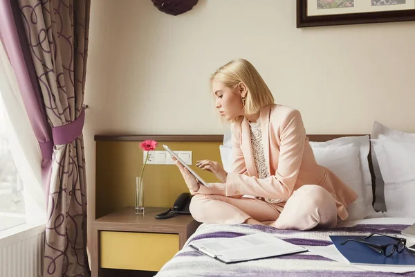 Businesswoman sitting on bed and using tablet