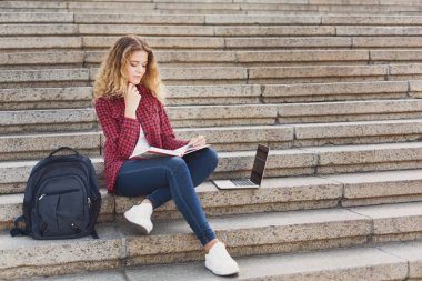 Dizüstü sıklıkta kullanarak merdivenlerde oturan gülümseyen kız öğrenci