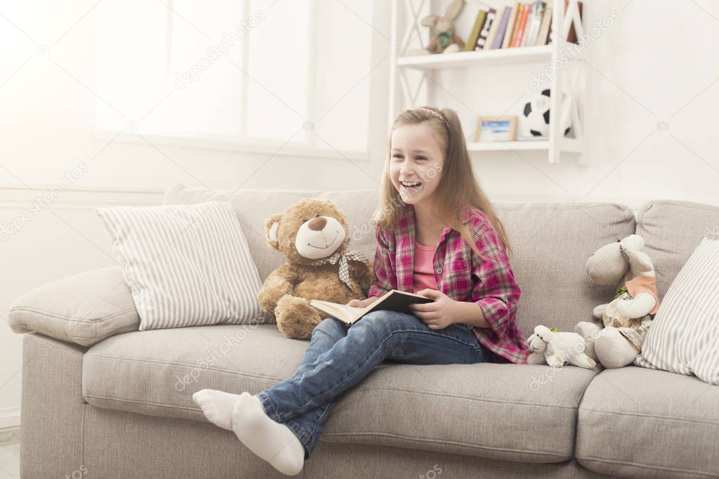 Happy little child reading book for her teddy bear