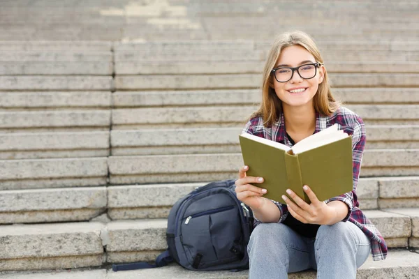 Jonge vrouw lezen boek op trappen van Universiteit — Stockfoto