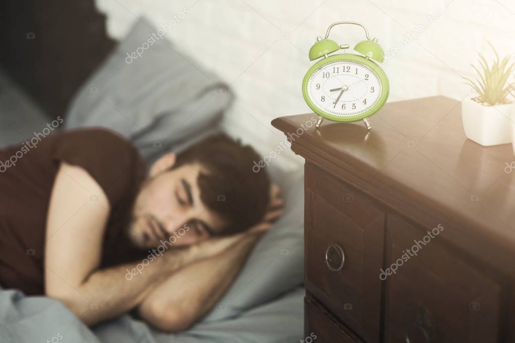 Sleeping man and clock in foreground in bedroom