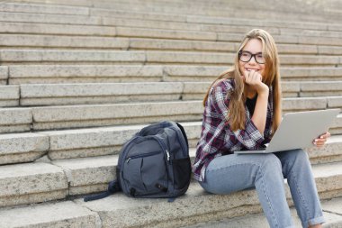 Gülümseyen öğrenci dizüstü kullanarak merdivenlerde oturan
