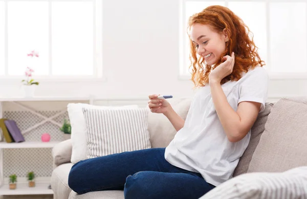 Chica feliz con prueba de embarazo sentado en el sofá —  Fotos de Stock