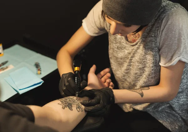 Mujer joven tatuadora haciendo tatuaje en brazo masculino — Foto de Stock
