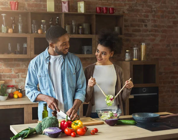 Loving afro american couple preparing green salad in kitchen