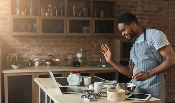 Black man baking pastry and using laptop in kitchen