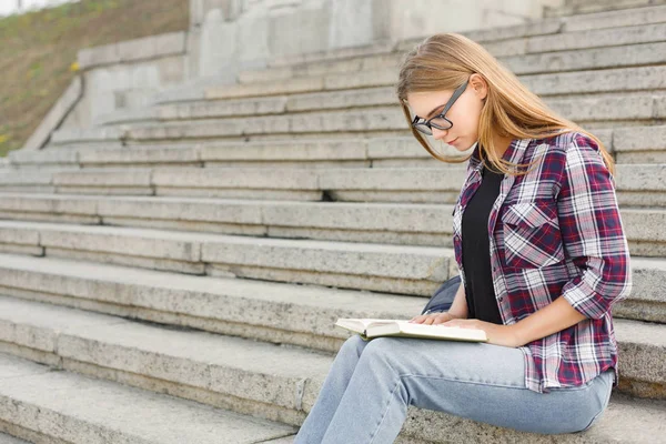 Genç kadın Üniversitesi merdivenlerde kitap okuma