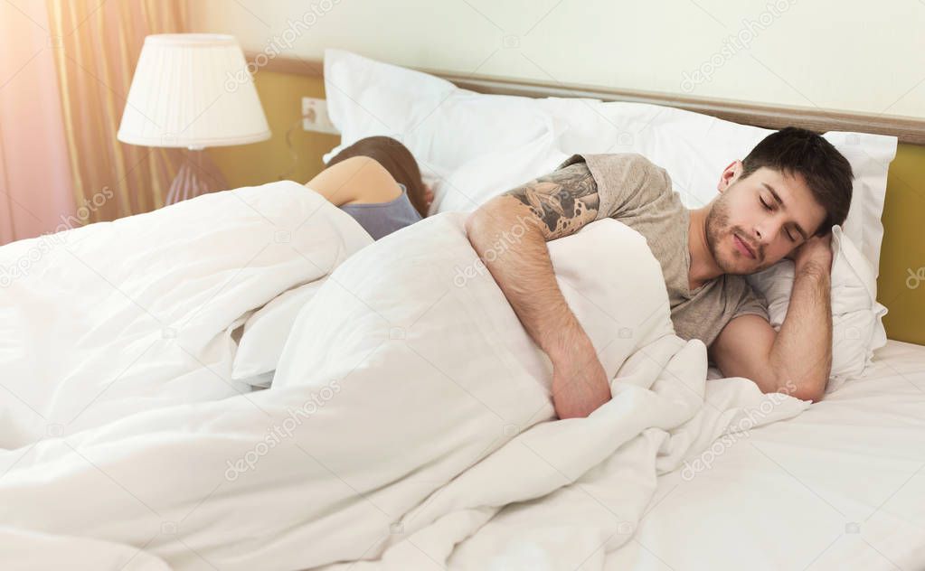Couple sleeping back to back in bed at home