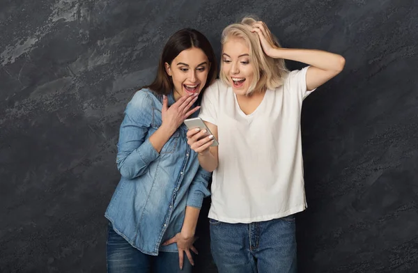 Verbaasd vrouwelijke vrienden met behulp van smartphone op donkere studio backgro — Stockfoto