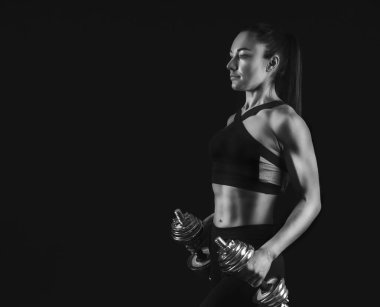 Kadın vücut geliştirmeci siyah arka plan, dumbbells ile