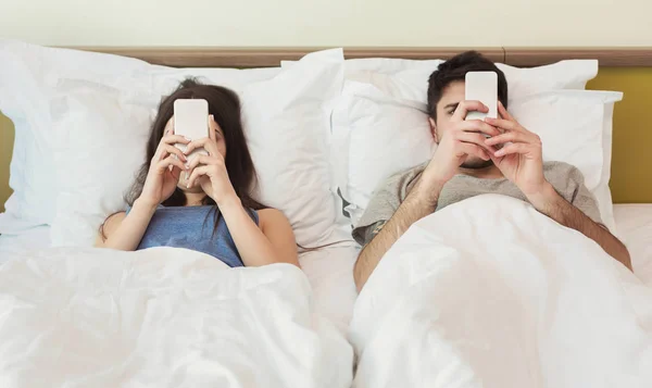 Pareja joven usando su teléfono móvil en la cama ignorándose mutuamente — Foto de Stock