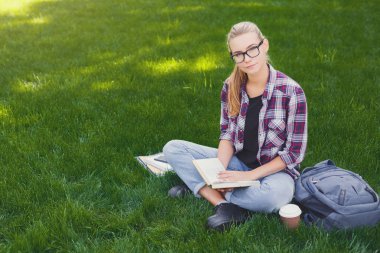 Parkta kitap okuyan genç bir kadın.