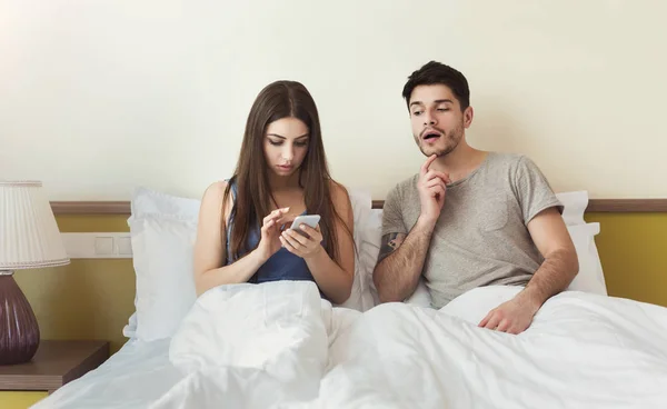Ревнивый муж смотрит на свою жену мобильный телефон на кровати — стоковое фото