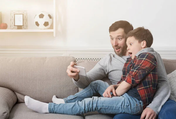 Pai engraçado e seu filho tomando selfie em casa — Fotografia de Stock