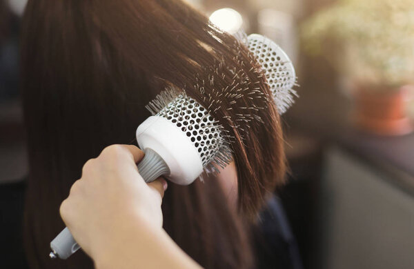 Hairdresser combing hair with round brush