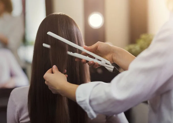 Парикмахер выпрямляет длинные каштановые волосы — стоковое фото