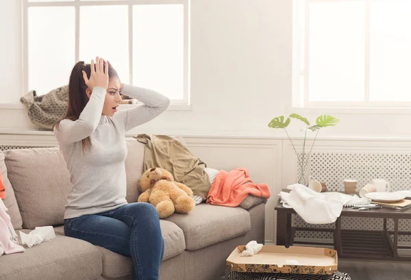 Desperate woman sitting on sofa in messy room — Stock Photo, Image